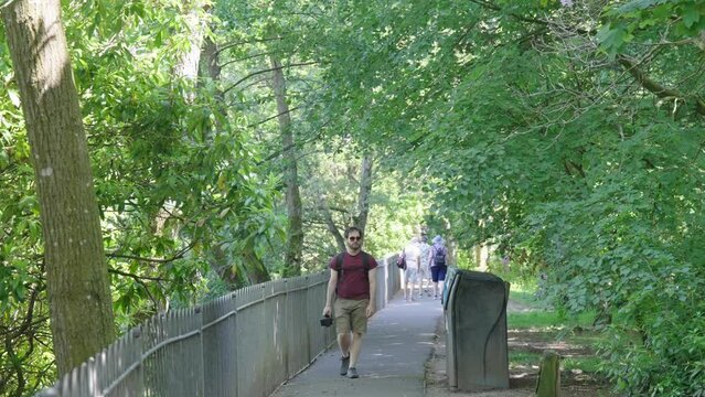 Man wearing sunglasses carrying a camera walking along a public path