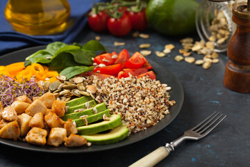 Salad with quinoa, avocado and chicken. Front view. Served on a black plate.
