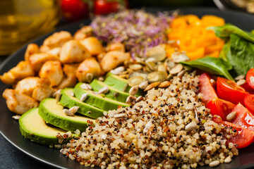 Salad with quinoa, avocado and chicken. Front view. Served on a black plate.