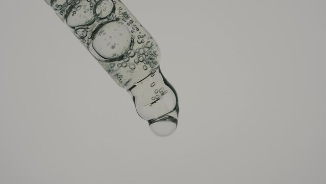 Transparent cosmetic gel liquid with air bubbles, oil or vitamin C in a glass pipette on a gray background. Macroscope.