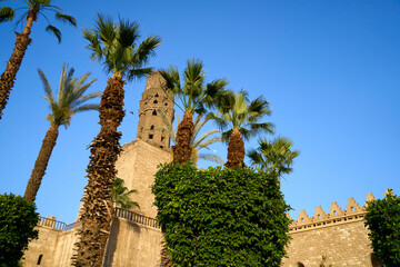 Obraz premium View of the tower through the trees from the square outside Al-hakim mosque in central Cairo, Egypt
