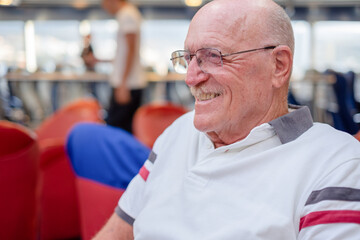 Portrait of smiling bald elderly man wearing glasses sitting inside ferry boat ready for crossing to La Palma island destination. Relaxed senior enjoys vacation and retirement
