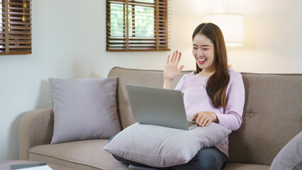 Women sitting on big sofa and greeting with friends in video call on laptop in lifestyle at home