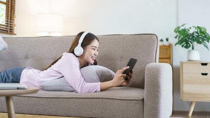 Obraz premium Women lying on big sofa and wearing headphone to watching movie on tablet in lifestyle at home