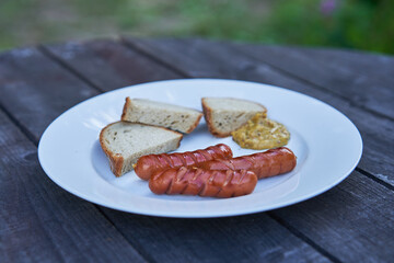 Roasted or grilled pork sausages served on white porcelain plate with slices of czech yeast bread and mustard outside on wooden table. Simple but tasty dinner typical for Czech or ´German cuisine.