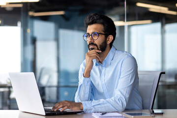 Serious thinking businessman inside office at workplace, mature Indian man in shirt working on...