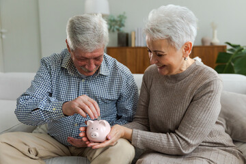 Saving money investment for future. Senior adult mature couple holding piggy bank putting money...