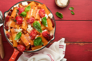 Pasta Tortiglioni with tomato sauce, baked cherry tomatoes, mozzarella and parmesan cheese, basil on old red rustic table. Traditional Italian cuisine. Example Italian food for article. Top view.