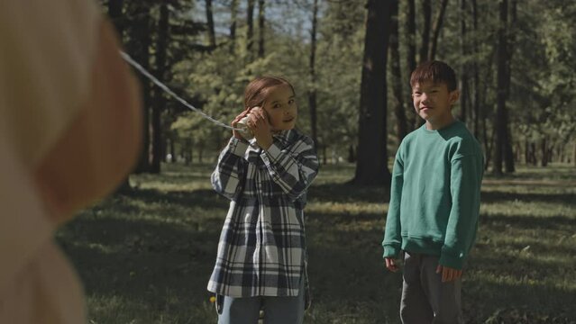 Little children having fun while playing with tin can telephone on summer day outdoors in park
