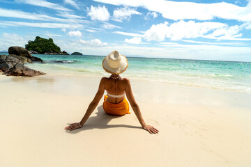 Rear view of beautiful woman in bikini and summer hat relaxing on the beach , on sea coast...
