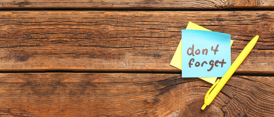 Sticky note with text DON'T FORGET and pen on wooden background with space for text