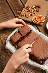 Woman cutting tasty chocolate brownie on wooden background