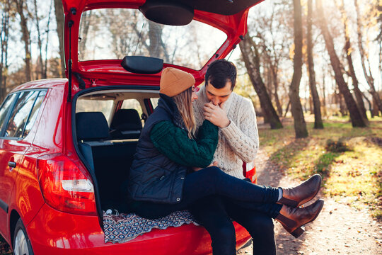 Happy loving couple relaxing in car trunk in autumn forest. Man kissing woman's hands. Travelling by auto.
