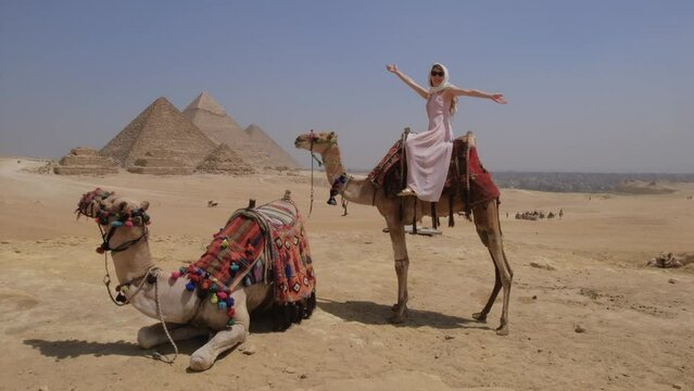 Young woman is sitting on a camel in Egypt. The Great Pyramids of Giza.