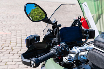 Part of a motorcycle steering wheel with various shift buttons and a rear view mirror. Close up.