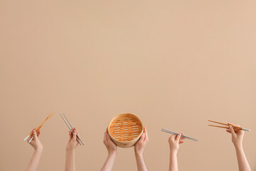 Hands holding different sets of chopsticks and bamboo steamer on brown background