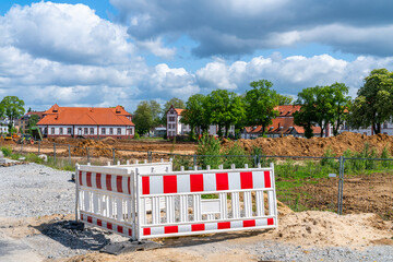 Earthworks at a construction site and a plot fenced with red and white barrier fence. The sky is...