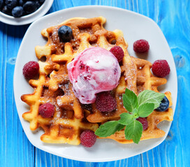 Waffles with ice cream and raspberries for breakfast over blue wooden table.