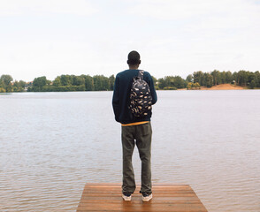 A young black man in sportswear with a backpack walks near the lake.