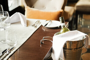 A bottle of white wine in ice bucket on the background of a served table in a restaurant