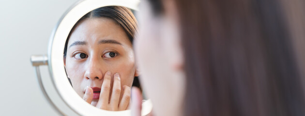 Young Asian woman looking in the mirror worried about the crack face skin and dark circle eyes.