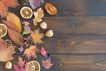 Autumn leaves, nuts, cones and slices of dried oranges on a brown wooden background. Autumn background. Flat styling. Copy the space.