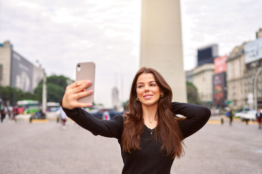 beautiful latin american woman taking selfie with a cellphone at the Obelisk of Buenos Aires