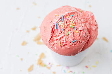 Overhead view of strawberry ice cream in white bowl on white table with wafer crumbs, horizontal, with copy space