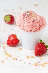 Top view of strawberry ice cream in white bowl on white table with crumbs and strawberries, vertical, with copy space