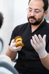 Stomatologist with glasses in latex gloves demonstrating metal dental braces on artificial human jaws skilled doctor explaining aligners effect on teeth correction in clinic