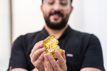 Obraz premium Orthodontist showing artificial human jaws from yellow plastic with installed metal braces for professional teeth correction doctor consulting patient in hospital