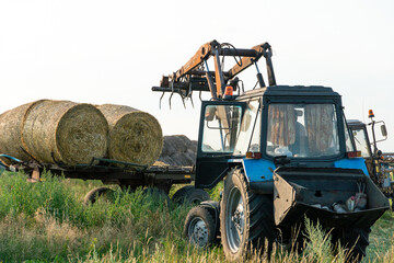 The blue tractor uses a hydraulic manipulator to stack round bales of hay in pyramids for storage...
