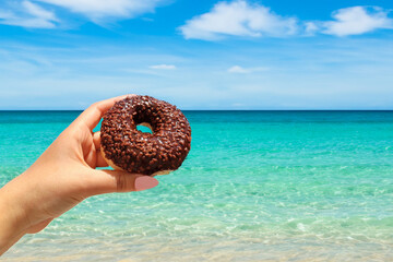 Donut. Hand holding a doughnut on the beach. 