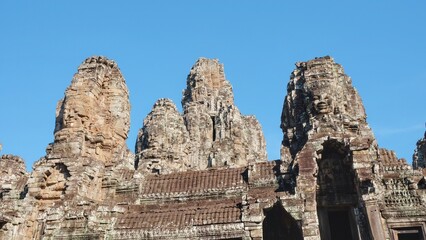 Image of the ancient Bayon Temple on a sunny day, displaying stone towers with human faces, located in Cambodia.