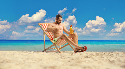 Man sitting on a deck chair and putting on sun lotion at the beach