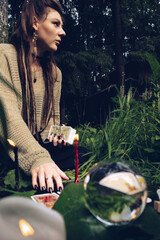 girl put her hands on the fortune telling table on a grass, where there are tarot cards, a ball for...