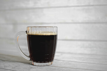 Fototapeta na wymiar a large faceted glass mug with cold dark beer on a light background. refreshing drink