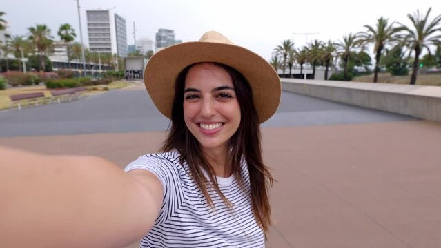 Happy young woman doing selfie video shot portrait with cell phone during summer vacation. Beautiful female tourist recording memories or sharing lifestyle moments on social media of her travel trip.