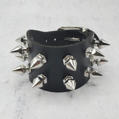 Black leather bracelet with spikes, holnitenes. An accessory for rockers, bikers, metalheads, goths and punks. Steampunk style. Close-up subject photography. - obrazy, fototapety, plakaty