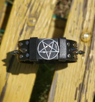 Black leather bracelet with spikes, holnitenes and a pentagram. An accessory for rockers, bikers, metalheads, goths and punks. Steampunk style. Close-up subject photography.