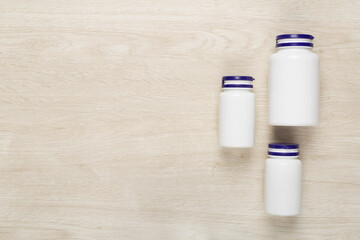 Plastic bottles with vitamins on wooden background, top view