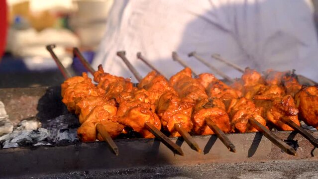 slow motion shot of tikka kebabs cooking over coal fire with smoke steam coming off showing a popular street food in delhi, lucknow india with chicken and mutton