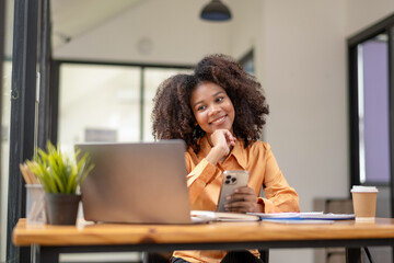 Obraz premium African American woman sitting in front of a laptop and holding a mobile phone.
