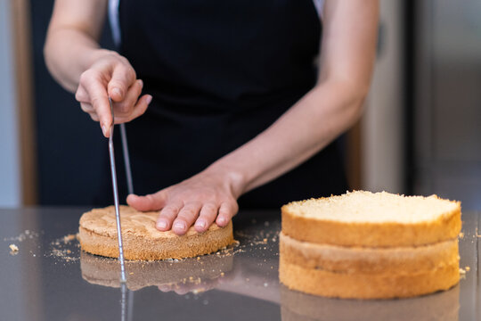 Professional confectioner making sugar free cake from natural ingredients in modern kitchen woman in black apron standing at table cutting baked dough with string knife