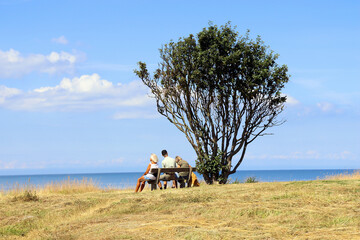 Obraz premium Natural and sea landscape. Family sits on a bench and looks at the sea.