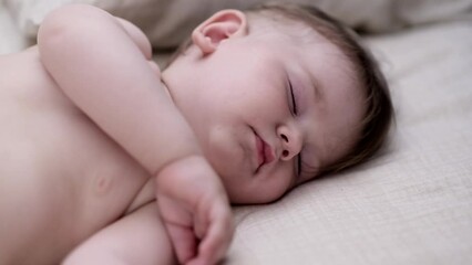Innocent little boy sleeping spreading hands on bed with white sheet in nursery tiny fingers of cute baby taking nap in afternoon after breastfeeding at home closeup