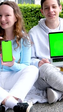 teen boy and teenage girl sitting outdoors with folders backpack holding laptop and phone green screen chroma key ad look here school presentation on computer. kid ready for video lesson