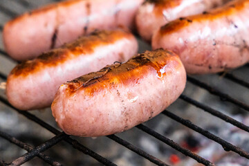 Group of delicious pink sausages on a black metal grille fried for a picnic are in a fireplace in the forest
