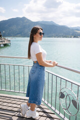 Side view of attractive young woman stand on bridge and look at big lake