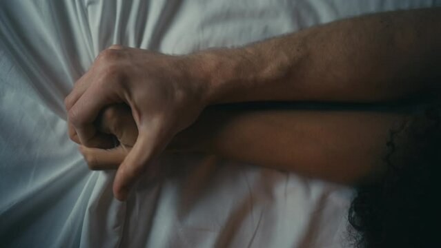 Closeup of young couple making love, passionately holding hands in bed, romance